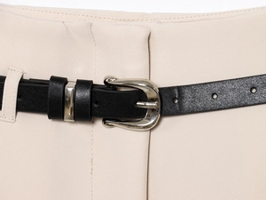 Macro detail of beige trousers featuring a black faux leather belt with a silver horseshoe buckle