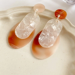 Detailed view of orange and white acrylic geometric earrings on a beige ceramic plate