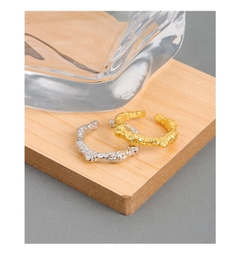Dettaglio di anelli in oro e argento con trama lavica su supporto in legno