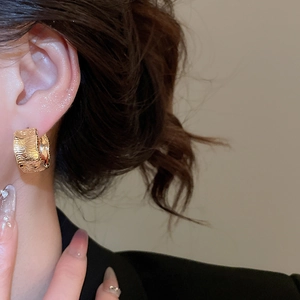 Macro detail of wide 18K gold plated hoop earring with luxury irregular bark texture