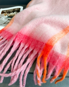 Close-up of soft pink and orange plaid scarf showing textured knit and long tassel fringe