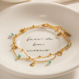 Double-layered gold anklet with turquoise beads and shell pendant on ceramic dish