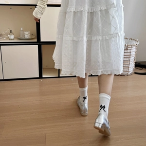 Close-up of white ankle socks with black bow detail paired with silver Mary Jane shoes