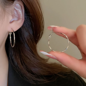 Detailed view of silver oval hoop earrings worn by a model showcasing polished finish