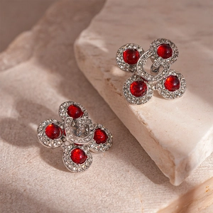 Retro clover earring with red resin and G-letter detail on a beige textured stone