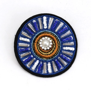 Detailed view of handmade Evil Eye brooch with blue beads and pearl center on white background