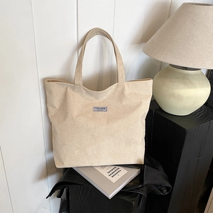 Detailed view of the ribbed corduroy texture and fashion label on the beige tote bag