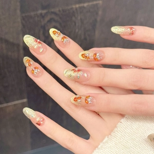 Detail van glitter goud druk-op nagels met oranje strass-steentjes in bloemmotieven