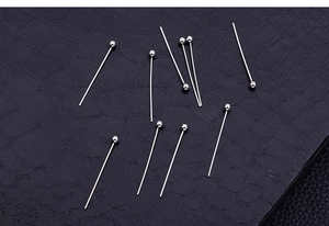 Macro shot of silver stainless steel ball head pins on textured black surface for DIY jewelry
