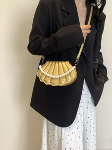 Detail of a golden shell-shaped crossbody bag featuring 3D textures and pearl chain accents
