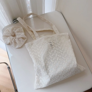 Close-up of cream lace embroidery texture on a tote bag with a matching hair scrunchie