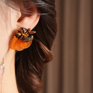 Close-up of vintage shell tiger eye earrings with orange translucent discs worn by model