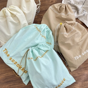 Flat lay of drawstring organizer bags in mint, khaki, and cream with embroidered text