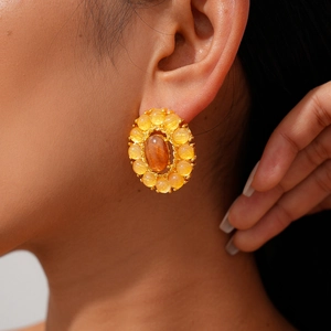 Primer plano de aretes ovalados geométricos con piedras de ámbar en la oreja de la modelo
