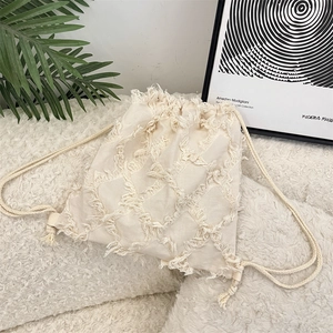 Detail of beige canvas backpack featuring bohemian tassel design and drawstring closure