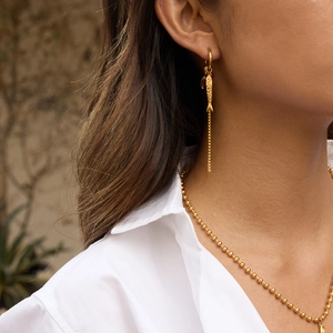 Detail of golden fish tassel earrings and matching necklace worn by a model in soft light