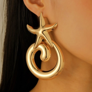 Close-up of oversized gold starfish spiral earrings on model for a beach holiday look