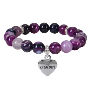 Détail d'un bracelet en perles d'agate violettes avec un pendentif cœur gravé