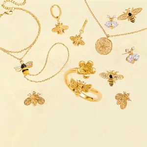 Golden bee and flower jewelry set with necklaces, earrings and rings on cream background
