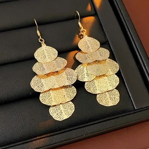 Detail of layered gold metal leaf earrings on a black cushion showing texture