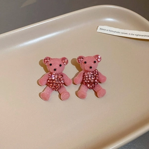 Close-up of pink flocked teddy bear earrings with rhinestone accents on a beige tray