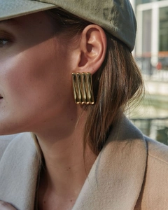 Close-up of gold plated ribbed rectangular stud earring worn on model's ear