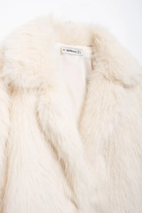 Detail view of cream faux fur coat collar with brand size label and fabric texture