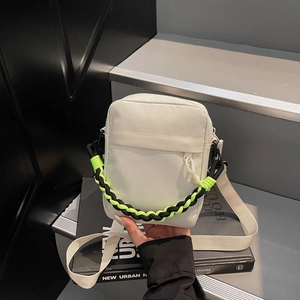 Detail of canvas crossbody bag showing front zipper pocket and neon woven handle cord