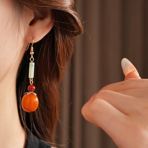 Close-up of model wearing orange persimmon drop earrings with green beads and gold finish