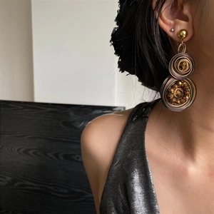 Detailed close-up of woven geometric spiral drop earrings with crystal beads on model