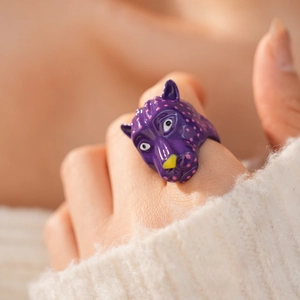 Gros plan d'une bague tête de léopard violette à pois roses sur un doigt.