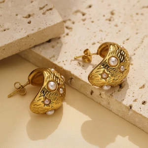 Detailed view of C-shaped golden earrings with baroque pearls and textured metal finish