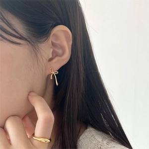 Close-up of elegant gold bow earrings and a minimalist gold ring worn by a model