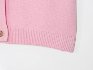 Dettaglio del maglione in maglia rosa con orlo a coste e bottone dorato su sfondo bianco