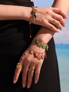 Detail of gold charms bracelets with colorful enamel pendants on woman against seaside