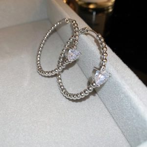 Detailed view of silver beaded hoop earrings featuring a heart-shaped crystal pendant