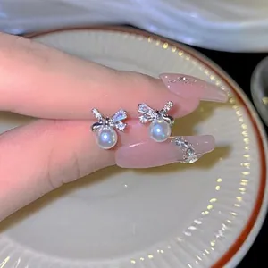 Detail of silver bow earrings with micro-paved crystals and round white pearl drop