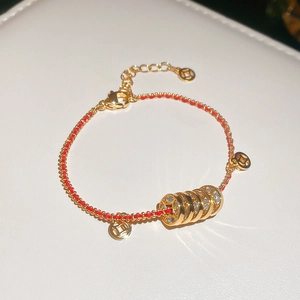 Dettaglio del bracciale in cordino rosso intrecciato dorato con ciondoli a moneta