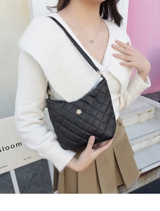 Close-up of black quilted shoulder bag featuring a gold flower emblem on a model