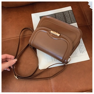 Détail du sac besace en cuir caramel avec boucle dorée sur un fond texturé aux tons chauds