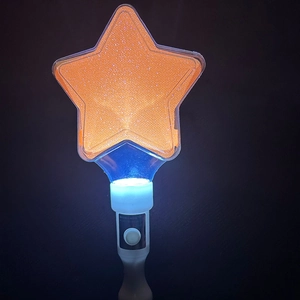 Close-up of orange star-shaped glowing concert stick with glitter and white handle