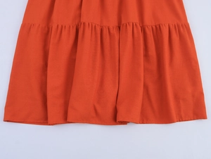Detailed macro view of orange V-neck dress featuring ruffled hem and pleated stitching