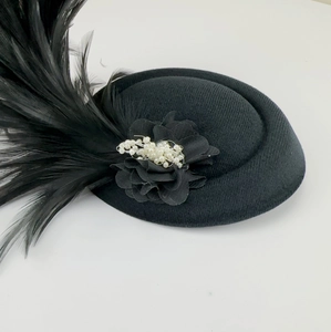 Close-up of a vintage black fascinator hat with large feather and pearl flower decoration.