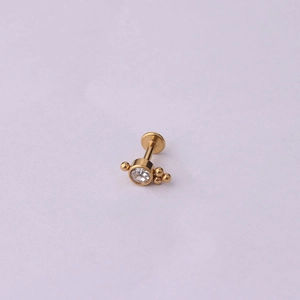 Détail d'un piercing labret doré orné d'une pierre claire et de petites perles