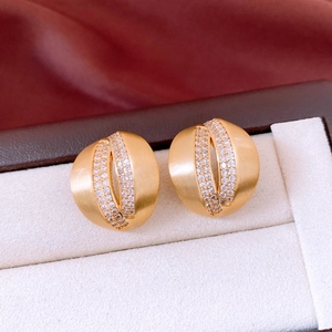 Detailed close-up of gold C-shaped earrings with micro-pave zircons in a jewelry box