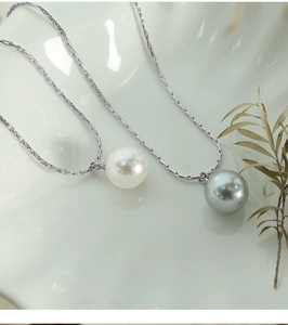 Detail of white and grey pearl pendants on silver snake chains over a ceramic plate