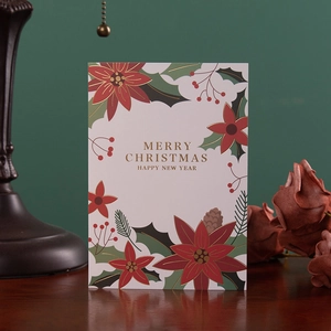 Premium Christmas card with gold foil lettering and festive pine patterns on a wooden table