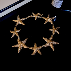 Detail der goldenen Seestern-Halskette mit strukturierten Metallanhängern auf Schwarz