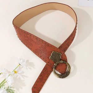 Brown leather punk belt with floral embossing and bronze buckle on beige background
