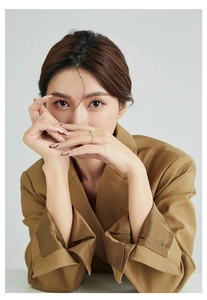 Close-up of a minimalist golden ring on a model wearing a brown suit jacket